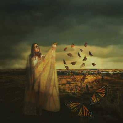 A young woman stands in a field. A butterfly's wings cover her eyes and a trail of butterflies fly to her outstretched hand.